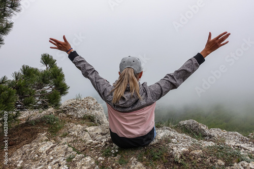 A picturesque mountain landscape in the clouds on Ai-Petri mountain in the Crimea. A woman on the background of a high-altitude landscape with trees in the clouds. Fog on the mountain.