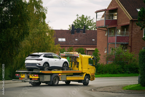 A car with a broken engine on the road, being towed by a truck to a repair shop, as part of the roadside assistance and vehicle recovery service.