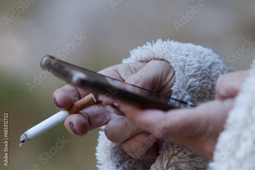 Manos de mujer adulta utilizando tecnología 5g en el movil mientras sujeta un cigarrillo encendido, Alcoi, España