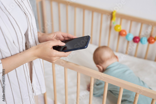 Close up of unrecognizable mother holding smartphone with blank screen while caring for baby boy and researching childcare, copy space