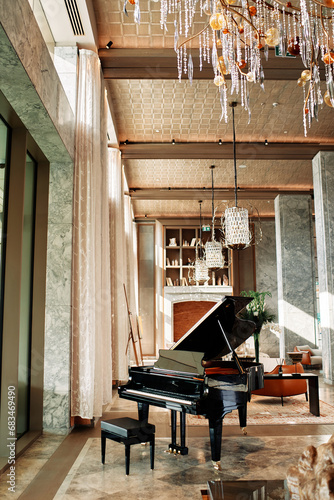 Black piano with a stool stands in a hotel lobby with modern chandeliers hanging from the ceiling