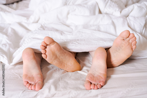 Feet of a couple in bed under the white blanket.