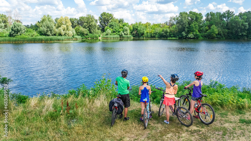 Family on bikes cycling outdoors, active parents and kids on bicycles, aerial view of family with children relaxing near beautiful river from above, sport and fitness concept 