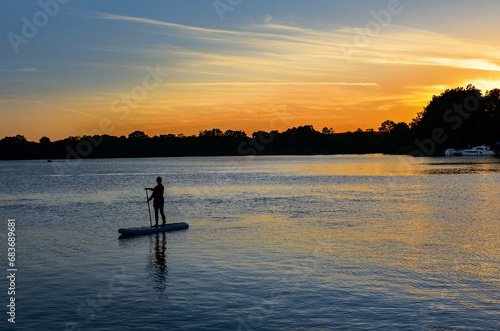 Girl paddling on SUP board on beautiful lake during sunset or sunrise, standing up paddle boarding morning adventure in Germany lake district Mecklenburg 