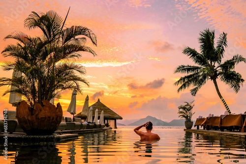 young men in a swimming pool during sunset, a Luxury swimming pool in a tropical resort, relaxing holidays in the Seychelles islands. La Digue, a Young guy during sunset by the swimming pool