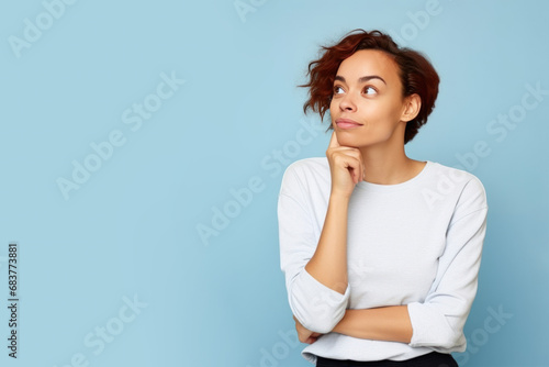 Jeune femme en train de penser en regardant sur le côté vers le haut, espace libre pour du texte ou mise en scène, tenue claire fond uni bleu pâle