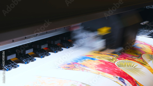 A moving working industrial wide format printer prints a color picture on paper.