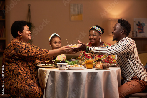 Smiling woman giving bowl of salad to her son-in-law to family dinner