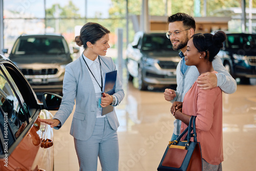 Happy saleswoman talking to couple who is buying new car in showroom.