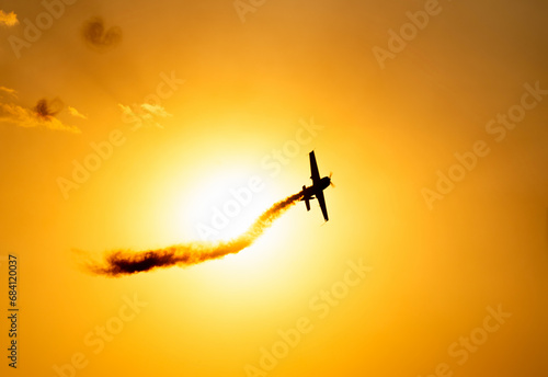 A silhouette of an aerobatic airplane flying at sunset against the crimson sky.