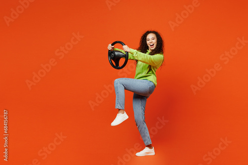Full body side profile view young woman of African American ethnicity she wears green hoody casual clothes hold steering wheel driving car isolated on plain red orange background. Lifestyle concept.