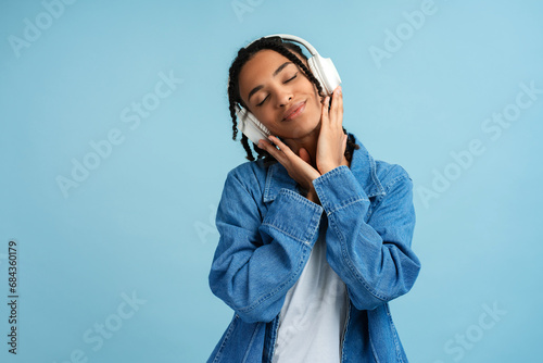 Happy African American woman wearing denim shirt with closed eyes listening to music in headphones