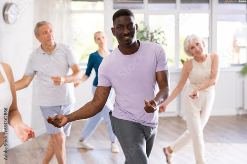 African American man is engaged in modern dance class with group friends of different age and learn to perform movements to rhythmic music.
