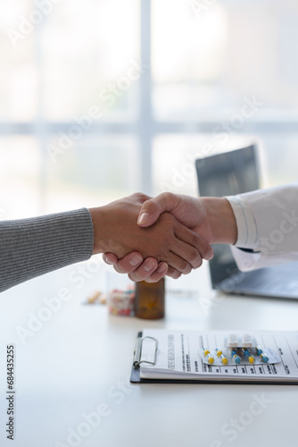 Medical service worker or doctor, pharmacist shaking hands with female medical patient at the table in clinic after giving advice on how to take medicine to the patient. Health care service concept.