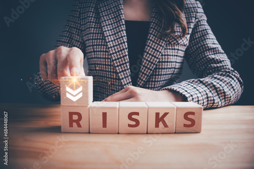 Businesswoman with word "RISK" on wooden blocks cubes and arrow pointing down. Risk reduction, business risk management, risk assessment, investment, planning strategies, achieving goals concept.