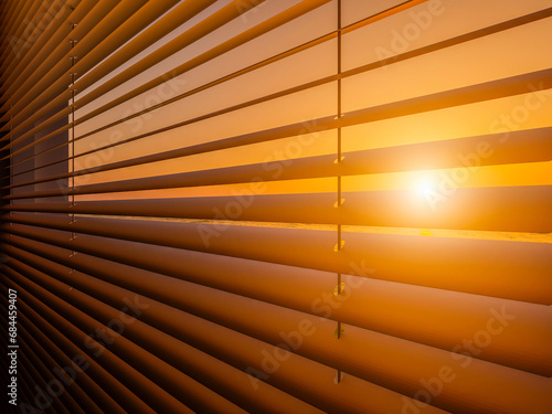 The setting sun shines through the closed horizontal blinds.