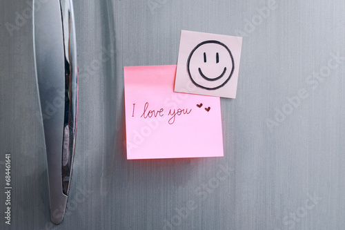 Sticky note with handwritten text I Love You attached to refrigerator door in kitchen. Romantic message.