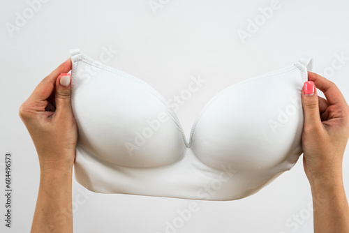 female hand is holding a hanger with a white bra lingerie isolated on light background