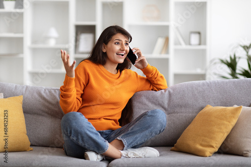 Emotional pretty young indian woman talking on phone at home