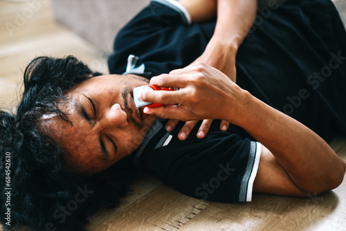 Young man with breathing difficulties using an inhaler during asthmatic attack on the floor