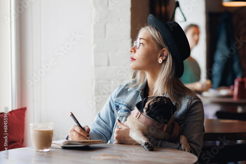 Lifestyle blogger woman working on web tablet with pug dog at pets friendly cafe. Outdoor lifestyle work with Pet from anywhere concept