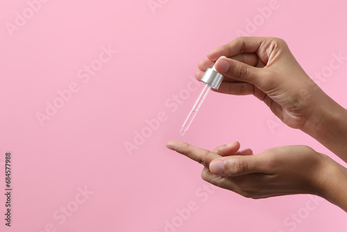 Woman applying cosmetic serum onto her finger on pink background, closeup. Space for text