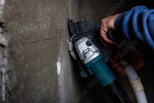 Worker holding angle grinder with two diamond discs for cutting grooves in wall.
