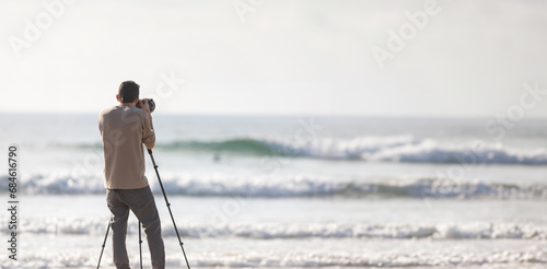 Young handsome photographer with a tripod and a camera on the beach