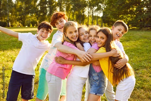 Children have fun and make friends at the summer camp. Group of kids spending time outdoors together. Bunch of happy girls and boys hugging each other in a green sunny park