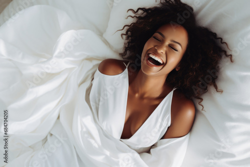 Image from top of happy woman 20s lying in bed on white linen and smiling