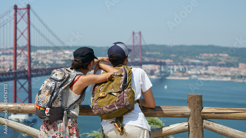 Tourists (young married couple) look at the suspension bridge over the Tagus River in Lisbon from the observation deck.