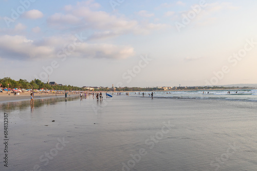 BALI, INDONESIA - OCTOBER 10, 2023: Tourists and locals on famous Kuta beach in Kuta, Bali. This is the perfect place for learning surfing.
