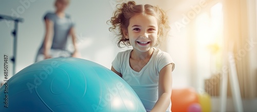 Girl receiving physiotherapy in a children s therapy center doing exercises on a gymnastic ball with physiotherapists for scoliosis prevention and treatment copy space image