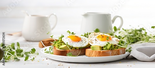 Healthy breakfast featuring avocado egg sandwiches and coffee served on a white table with whole grain toasts mashed avocado fried eggs and organic microgreens copy space image