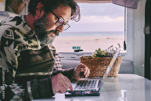 Working off grid in alternative office and online job lifestyle concept man. Adult people work on a laptop inside a camper van motor home. Smart working in travel vehicle transport. Using notebook