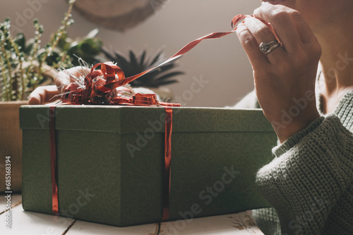 Close up of a woman unpacking a surprise gift box. Christmas or birthday anniversary present. Female people celebrate at home with a package and red tape. Green color mood image. Sharing gift moment