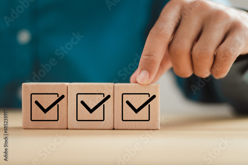 Checklist survey concept. Man hand putting wooden cube with checklist icon. Survey checklist, assessment, quality control.