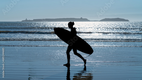 Silhouette of an unidentified man with a surf board, walking in the beach of Essaouira, Morocco, which offers a perfect blend of wind and waves, attracting surf enthusiasts from around the world