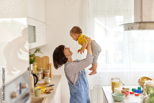 Mother lifting up her baby boy in the air in the kitchen