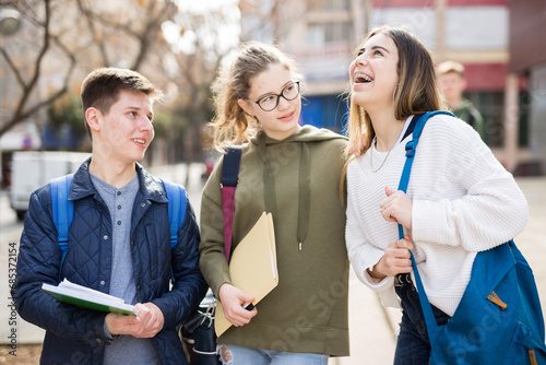 Carefree teenage friends friendly talking near college building after lessons in sunny day