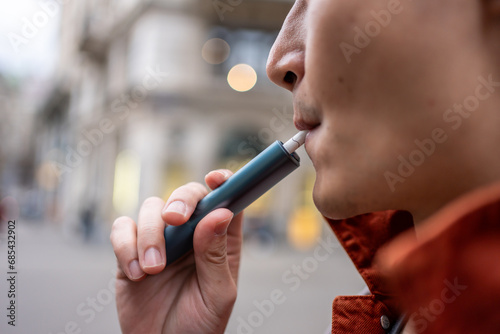 Close up of a man vaping with electronic cigarette outdoor on street.