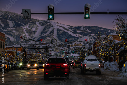 View of main street in Colorado resort town decorated for charismas at night in winter; mountain with ski runs in background