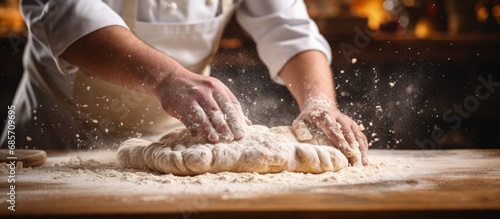 Close up of artisan baker sprinkling flour on fresh dough in rustic bakery kitchen Copy space image Place for adding text or design