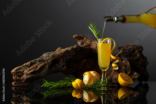 Traditional Italian liqueur Limoncello on a black reflective background.