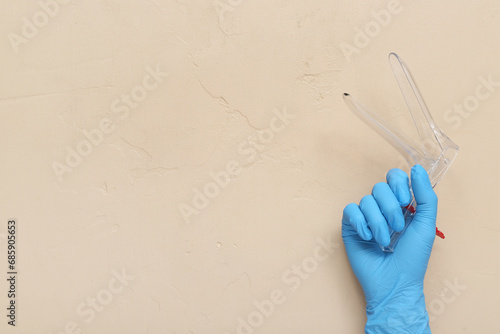 Hand in medical glove and with gynecological speculum on beige background