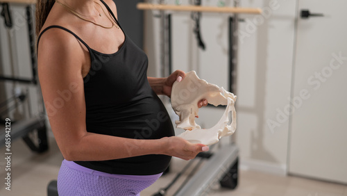 Pregnant woman holding sample of pelvic bones in yoga studio. 