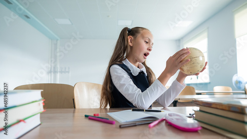 Caucasian schoolgirl sits at her desk at school and studies the globe. 