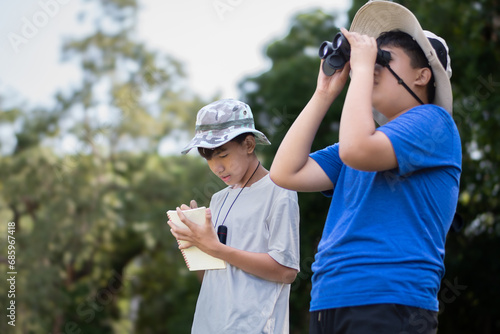 Asian boys holding binoculars and watching birds which fying on sky, insects, forest animals and living things which crawling and jumping on the branches and on the underside of trees in tropical park
