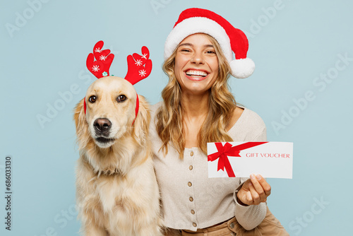 Young happy owner woman with wears casual clothes Santa hat hug best friend retriever dog hold store gift certificate coupon voucher card isolated on plain blue background. New Year discount concept.