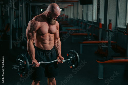 Caucasian bald topless man doing an exercise with a barbell in the gym. Bicep curls with weights.